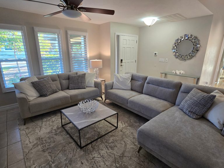 Frokopiertes Wohnzimmer mit grauem Sofa, Tisch und großer Fensterfront.